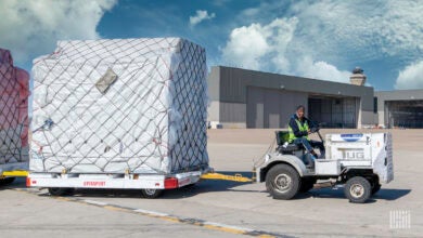 A small ground tug pulls a large pallet with wheels at an airport.