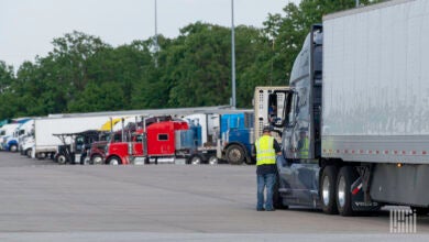 A man in a neon vest speaks to a semi truck driver through the driver side window.