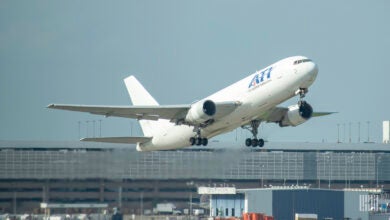 A white ATI freighter takes off with the airport buildings behind it.