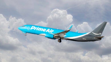 A light-blue Amazon Prime Air cargo jet flies takes off through the clouds.