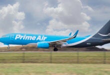 A light blue Prime Air cargo jet for Amazon lands on a runway.