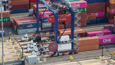 Image shows shipping containers, cranes, trucks and pavement.