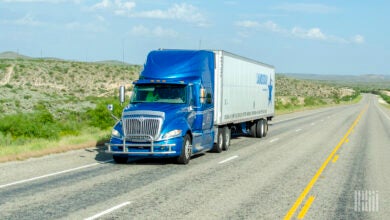 A blue tractor pulling a Landstar trailer on a highway