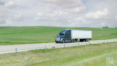 A grey tractor pulling a white dry van trailer on a highway