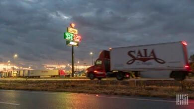 A red Saia daycab pulling a pup trailer near a truckstop at night