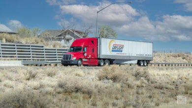 A red tractor pulling a white Daylight Transport trailer on a road with houses in the background