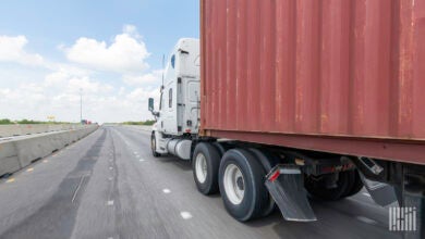 A white tractor pulling a rust-colored ocean container