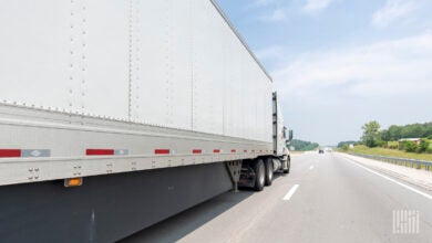 A white tractor pulling a white trailer on a highway