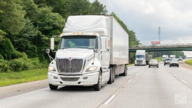 A white tractor pulling a white trailer on a highway