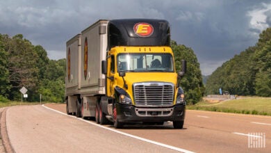 A yellow and black Estes day cab pulling two Estes pup trailers on a highway