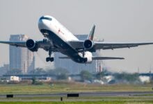 An Air Canada jet with black belly lifts off runway, coming toward viewer.