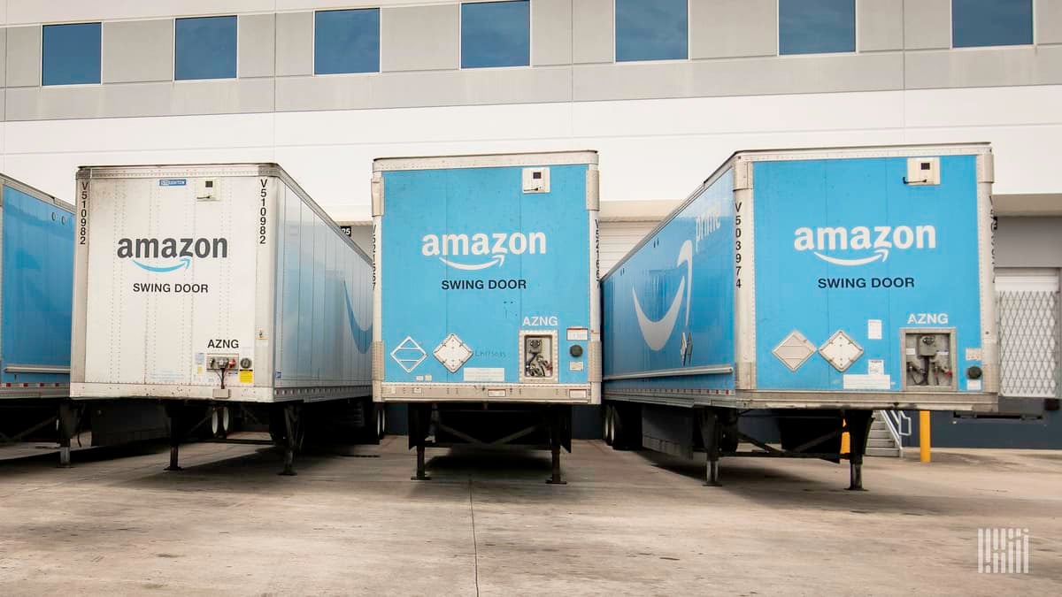 Blue Amazon truck trailers backed up to warehouse dock door waiting for a tractor to haul them away.