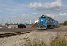 Image shows locomotives, ocean vessel, cranes.