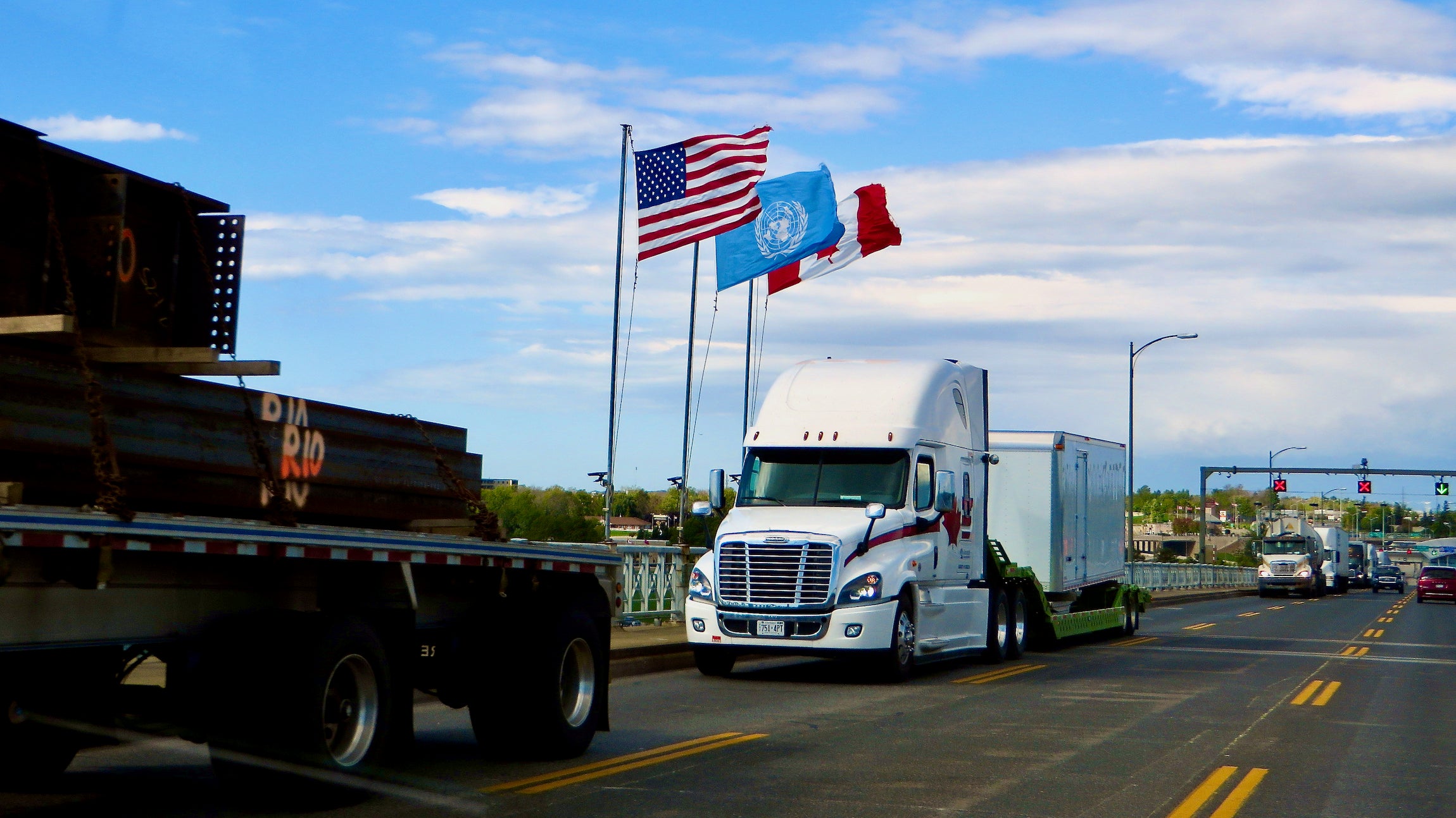 A tractor-trailer passes by a US, Canadian and United Nations flagl