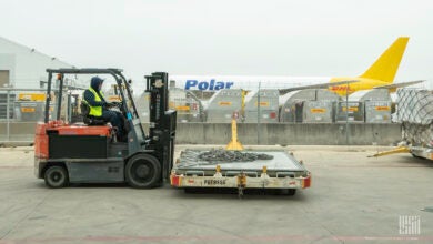 A forklift moves an empty pallet in foreground; a Polar Air Cargo freighter with yellow tail in background.