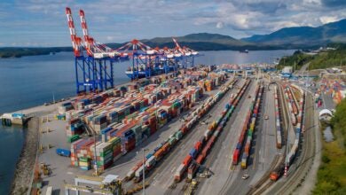 Image shows marine container terminal, cranes, stack trains, land forms and water.