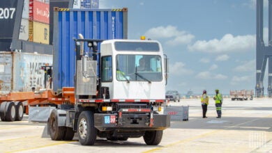 A yard tractor pulls a container on a chassis at a port.