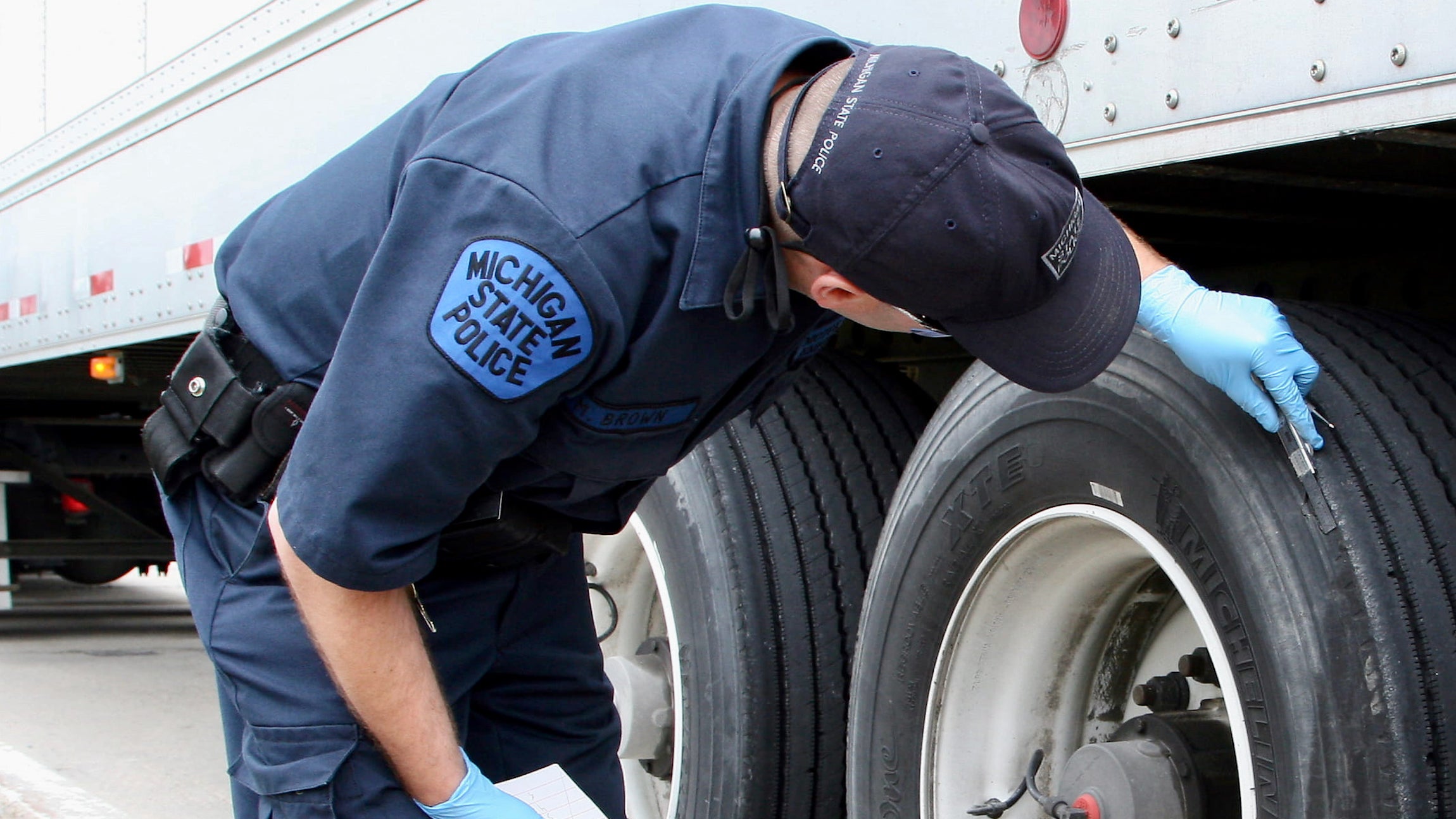 A Michigan state police officer inspects the wheel of a commercial truck.