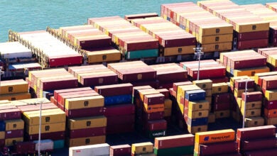 Image shows stacks of shipping containers and ocean.