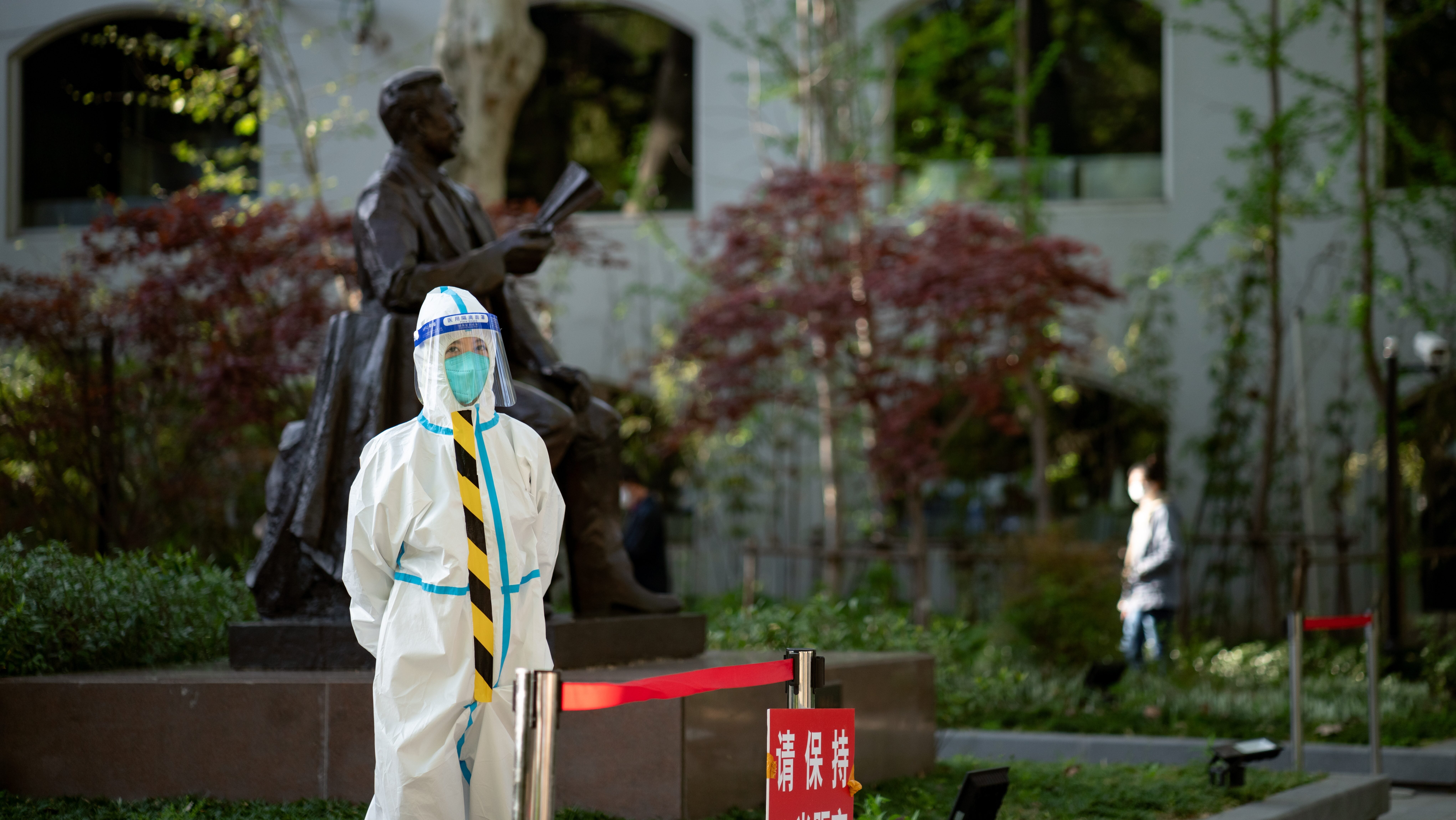 A person in white hazmat suit stands in front of a statute.