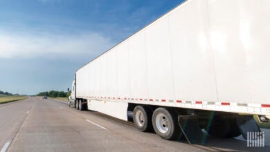 Side view of a white tractor pulling a white dry van trailer on a highway.