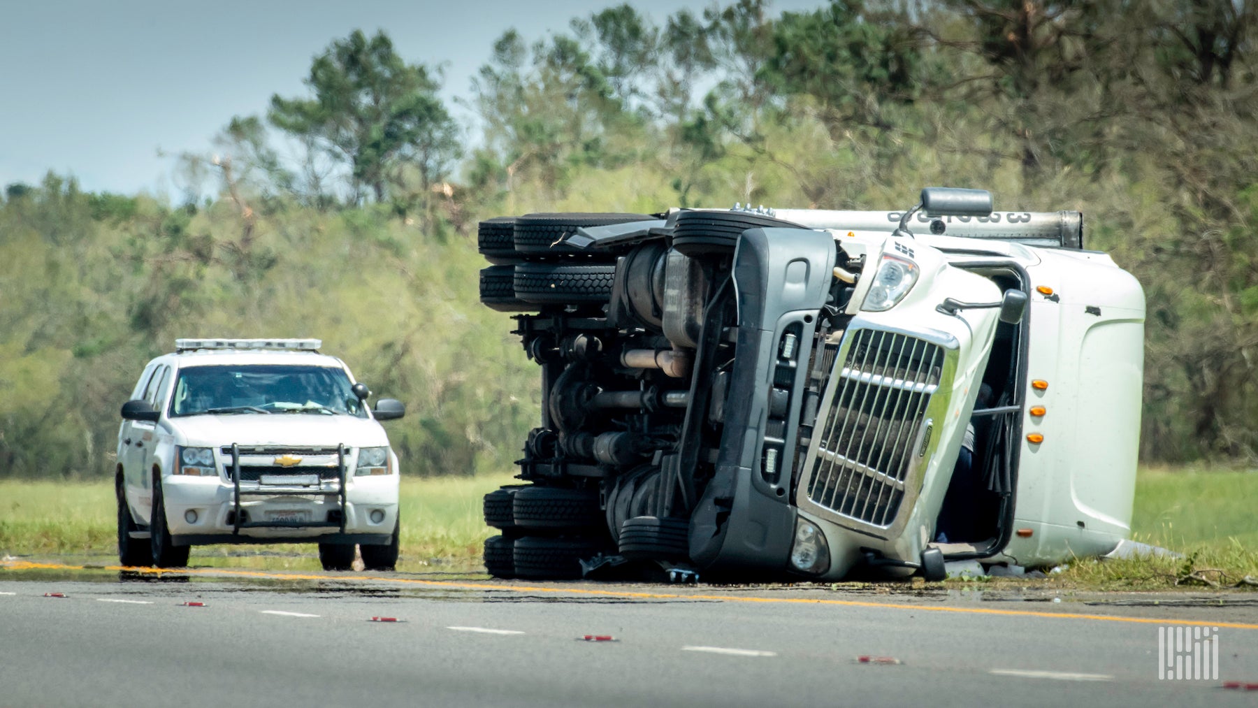 A white commercial truck sits on its side after a crash with a police car parked behind it.