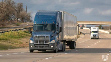 A blue tractor pulling a silver trailer on the highway